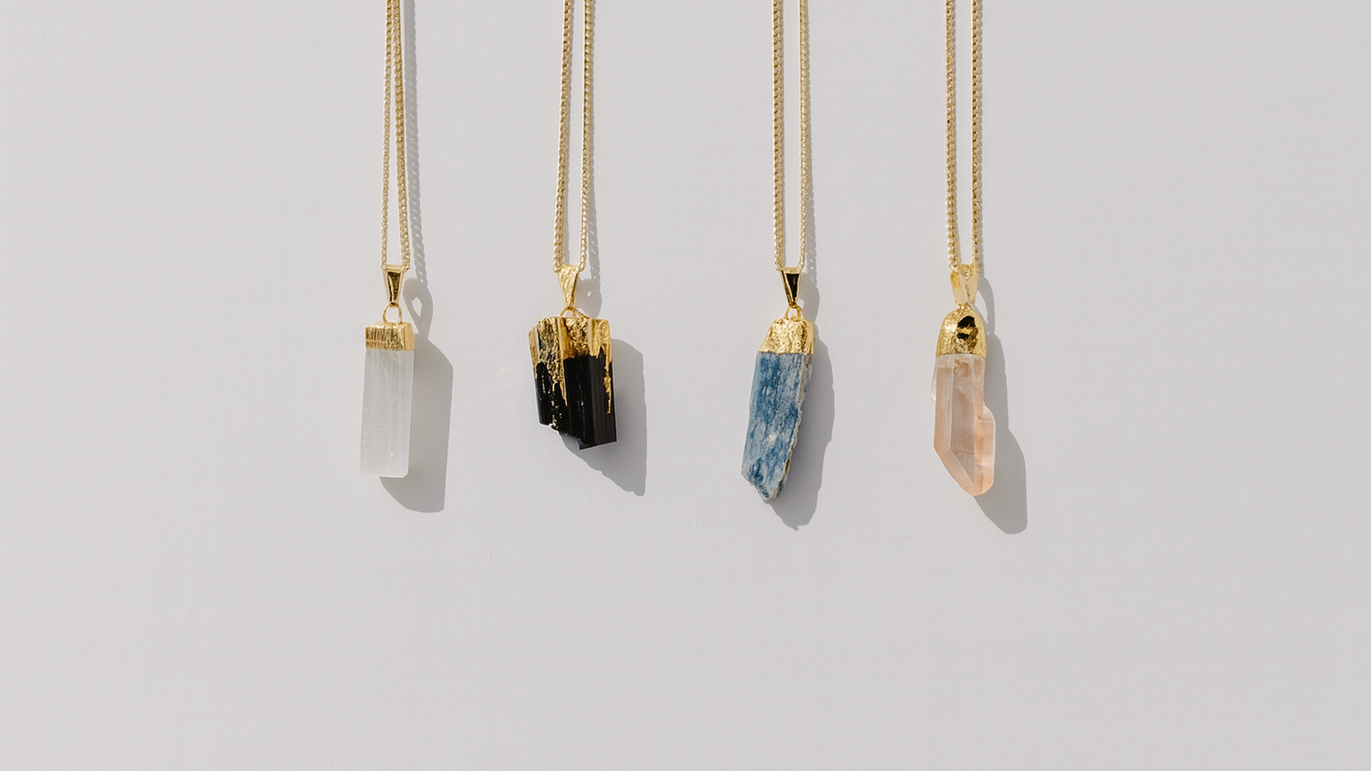 Four gold necklaces with crystal pendants on a light gray background